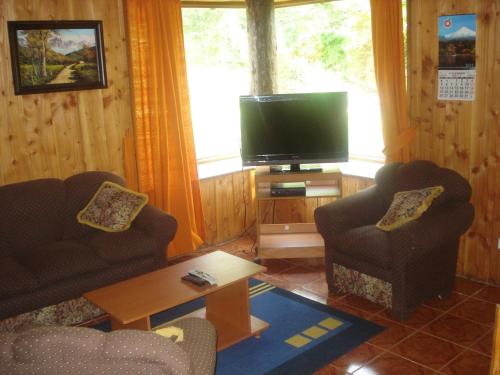 a living room with two chairs and a flat screen tv at Cabañas Pichares in Caburgua