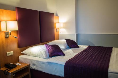 a hotel room with a large bed with purple pillows at City Hotel Niederrad in Frankfurt