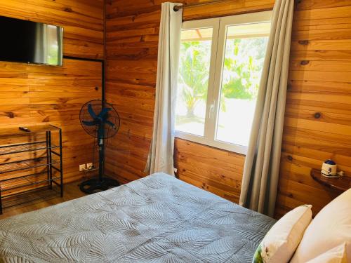 um quarto com paredes de madeira e uma cama com uma janela em Bungalow KURA em Moorea