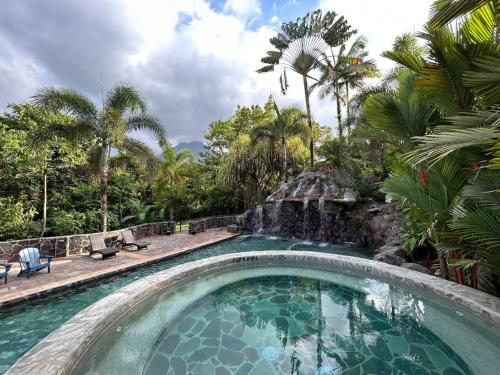 uma piscina com cascata e palmeiras em Luxury Cabin with Jacuzzi and Pool in La Fortuna em La Fortuna