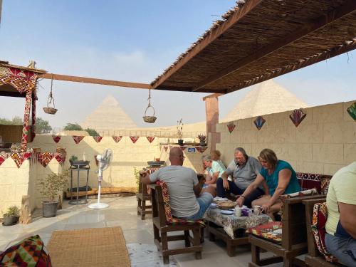 a group of people sitting on a patio with pyramids in the background at Pyramids Lounge Guest House in Cairo