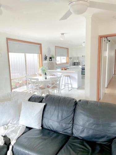 a living room with a leather couch and a kitchen at Coastal Springs - PET FRIENDLY & 200m To Beach! in Clifton Springs