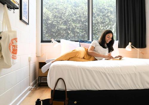 a woman sitting on a bed reading a book at The Village North Melbourne in Melbourne