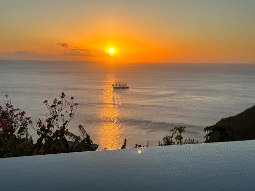a sunset over the ocean with a boat in the water at Infinity Luxury Villa - Stunning Sea and Piton Views in Soufrière