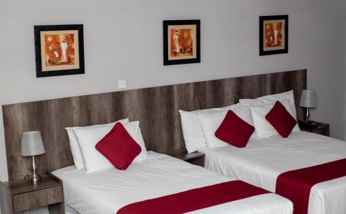a bedroom with two beds with red pillows at Platinum Hotel in Gaborone