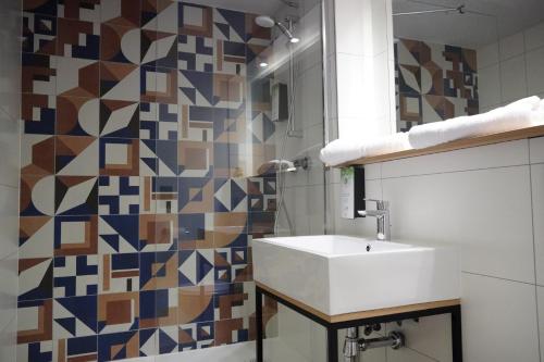 La salle de bains est pourvue d'un lavabo blanc et d'un mur en mosaïque. dans l'établissement Campanile Mulhouse - Illzach Ile Napoléon, à Illzach