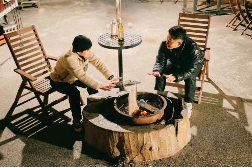 deux hommes sont assis autour d'un foyer extérieur dans l'établissement The Galaxy Express Nahama ザ・ギャラクシー・エキスプレス・ナハマ, à Yokosuka