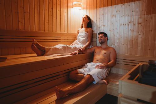 a man and woman sitting in a sauna at Spa & Wellness Hotel Fitak**** in Liptovský Ján