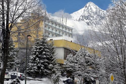 a building with a snow covered mountain in the background at Hotel SOREA URÁN in Vysoke Tatry - Tatranska Lomnica.