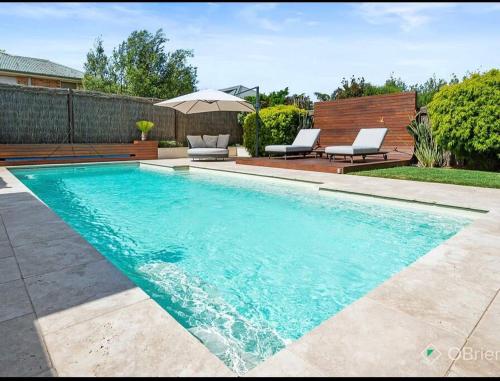 a swimming pool with two chairs and an umbrella at Luxury Family Holiday Rental On the Mornington Peninsula in Frankston South