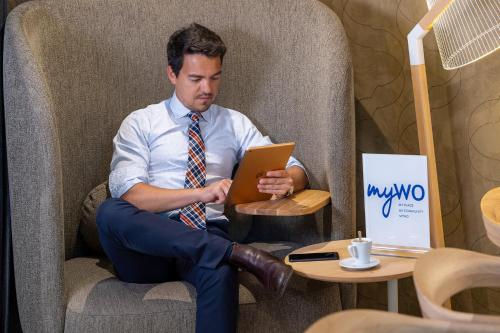 a man in a tie sitting in a chair with a tablet at Best Western Plus Hôtel Isidore in Saint-Jacques-de-la-Lande
