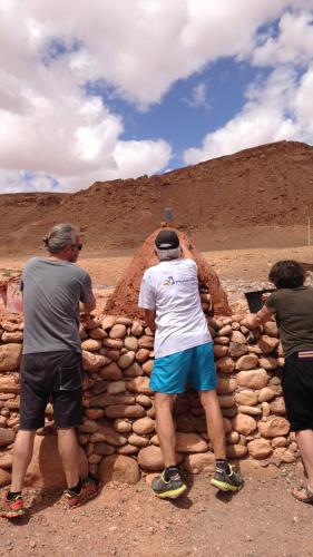 three men standing next to a stone wall at Tigmi Hamid Découverte des traditions et de la culture berbère in Aït Ben Haddou