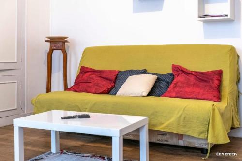 a yellow couch with red pillows and a white table at Le Baldaquin quartier cathédrale-marais in Bourges