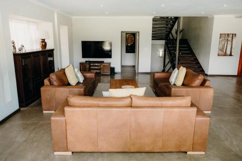 a living room with brown leather couches and a television at Ruzelle Family House in Hazyview