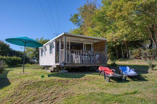 une petite maison avec un porche et un parapluie vert dans l'établissement Camping Brin d'Amour, à Les Eyzies-de-Tayac