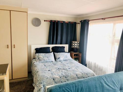- une chambre avec un lit doté de rideaux bleus et d'une horloge dans l'établissement Charming retreat in Danabaai, à Mossel Bay