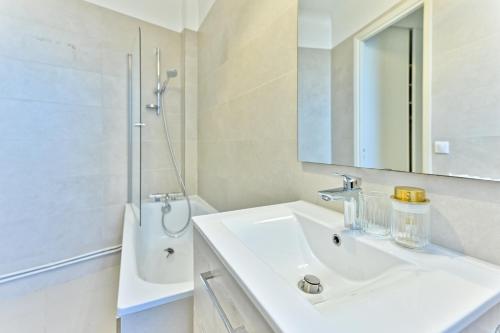 une salle de bain blanche avec un lavabo et un miroir dans l'établissement Apparement à 5 minutes de Paris - Neuilly, à Neuilly-sur-Seine
