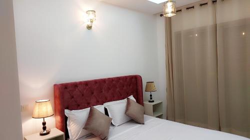 Appartement Perla - Costa Bouznika في بوزنيقة: غرفة نوم بها سرير مع اللوح الأمامي الأحمر ومصباحين