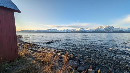 a red building next to a body of water with mountains at Villa Lyngenfjord in Olderdalen