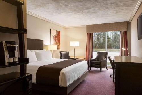 a hotel room with a bed and chairs and a window at Atlantic Host Hotel, Trademark Collection by Wyndham in Bathurst