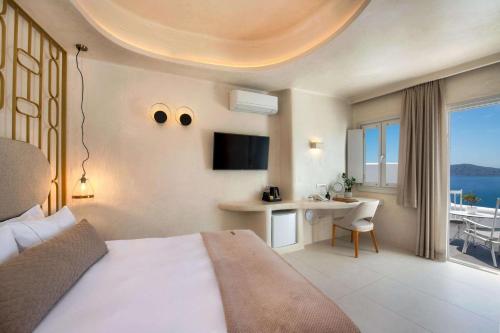 a bedroom with a bed and a desk and a television at Athina Luxury Suites in Fira