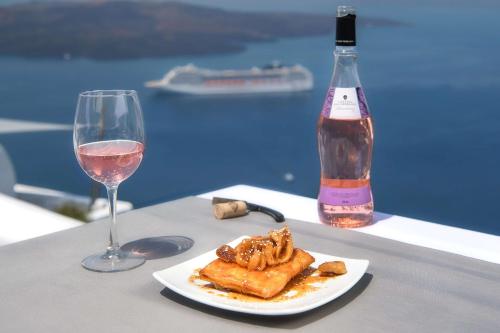 une assiette de nourriture et un verre de vin sur une table dans l'établissement Athina Luxury Suites, à Fira