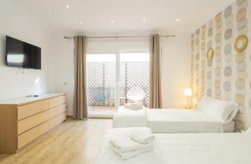 a white bedroom with two beds and a television at Cubo's Beach Side Apartment at La Cala in La Cala de Mijas
