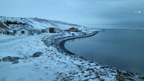 a snowy beach with houses and the water at Tangahús Guesthouse in Borðeyri