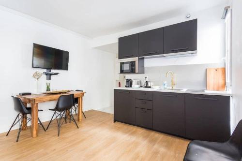 une cuisine avec des armoires noires et une table avec des chaises dans l'établissement Lemoine/Reaumur 1: Cosy Appartement 4P-1BR, à Paris