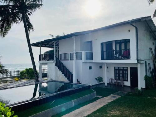 a white house with a swimming pool next to the ocean at Rainbow Surf Beach in Koggala