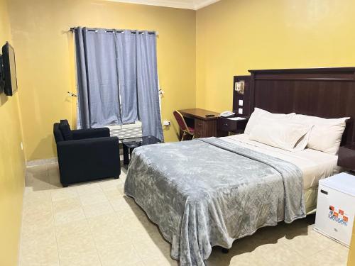 a bedroom with a bed and a chair and a window at Enclave Hotel Abuja in Kagini