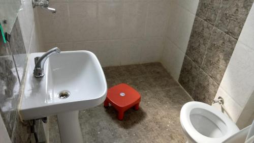 uma casa de banho com um lavatório, um WC e um banco vermelho em Bayweaver nests homestay in Royal plaza 810 em Lucknow