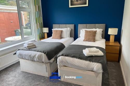 2 camas en una habitación con una pared azul en 3 Bedroom Cosy Bungalow By Beds Away Short Lets & Serviced Accommodation Chalgrove With Outdoor Dining Area, 