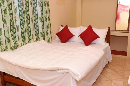 uma cama branca com duas almofadas vermelhas em Archu Agam em Kotagala