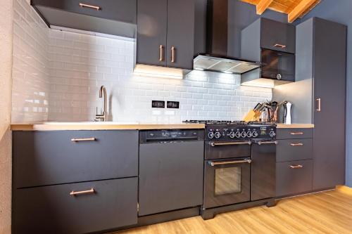 une cuisine avec des appareils électroménagers en acier inoxydable et des armoires noires dans l'établissement Le petit Paradis, chalet au coeur des 3 vallées, à Saint-Marcel