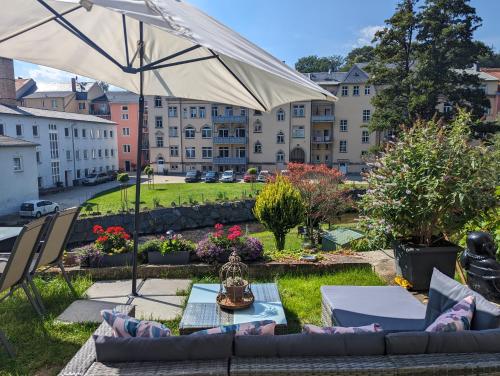 a patio with a couch and an umbrella at HW2B - Urlaubsmagie - Wohlfühlwohnung mit Balkon, Pool, Sauna & Terrasse in Sebnitz
