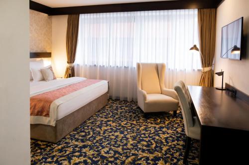a hotel room with a bed and a chair and a desk at Malak Regency Hotel in Sarajevo