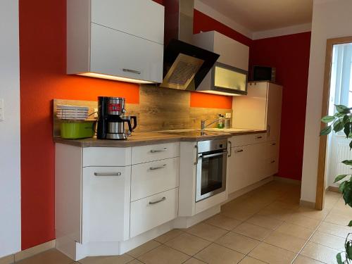 uma cozinha com armários brancos e uma parede laranja em Haus am Kölpinsee App 4 1 em Kölpinsee