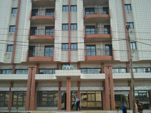 Un grand bâtiment avec des gens qui marchent devant lui dans l'établissement MAKO PALACE Hôtel, à Bafoussam