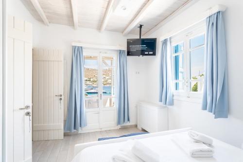 a white bedroom with blue curtains and a window at Luxury Sea House By Blue Waters Mykonos in Ornos