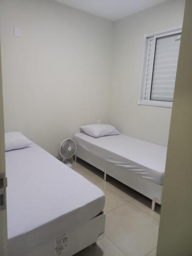 two beds in a white room with a window at Apartamento próximo ao centro com elevador! in Patos de Minas