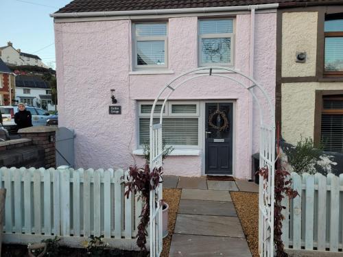 Uma casa cor-de-rosa com uma cerca branca à frente. em Charming 1-Bed Cottage in Brynmenyn em Bridgend