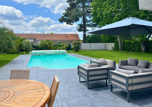 une piscine avec une table, des chaises et un parasol dans l'établissement La Villa Capucine, à Biscarrosse