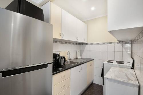 Una cocina con gabinetes blancos y un refrigerador de acero inoxidable. en Fly Around Town in Pocket Rocket, en Albion