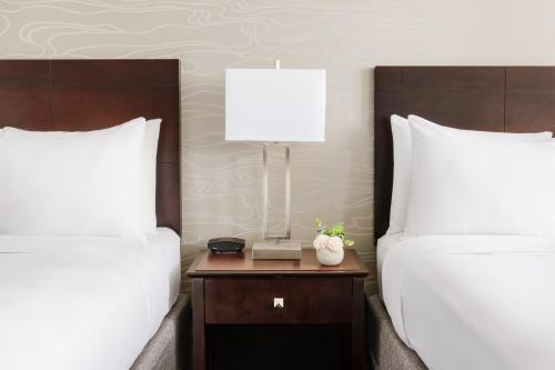 two beds with white pillows and a table with a lamp at Crowne Plaza Phoenix Airport - PHX by IHG in Phoenix