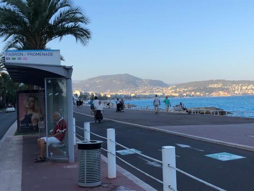 a man sitting at a bus stop near the beach at Vue mer, 2 pièces lumineux in Nice