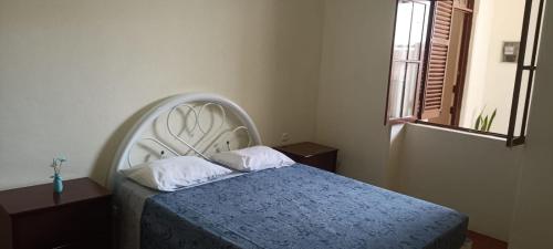 a bedroom with a bed with a blue blanket and a window at Hostel Mindelo in Mindelo