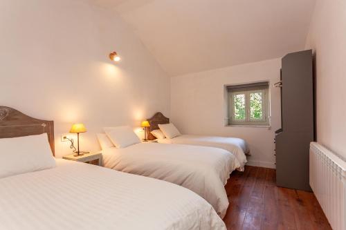 Habitación con 3 camas, sábanas blancas y ventana. en Caserío El Ronzón, en Camoca de Abajo
