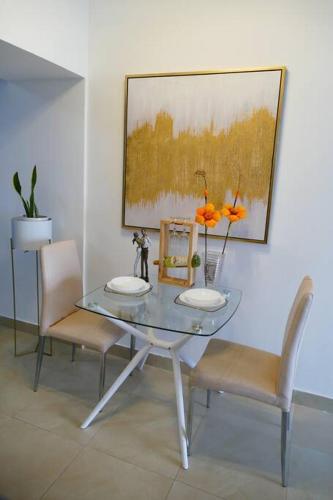 a glass table with two chairs and a painting on the wall at Ecusuites Penthouse Vía Costa Ceibos Puerto Azul in Guayaquil