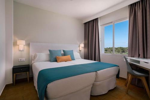 a hotel room with a bed and a desk and a window at AluaSun Mediterráneo in S'Algar